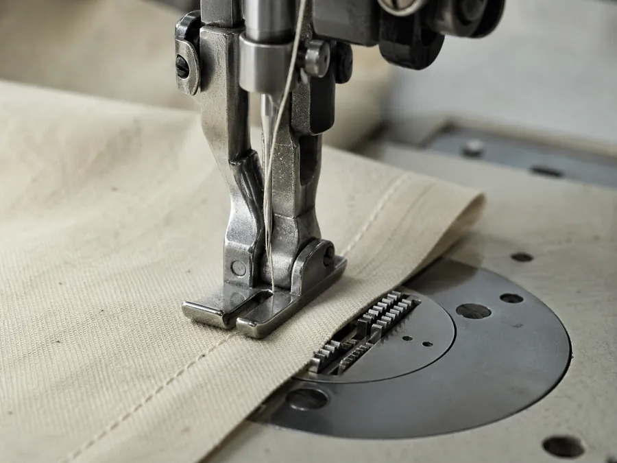 An industrial sewing machine foot mid-stitch on a plain seam